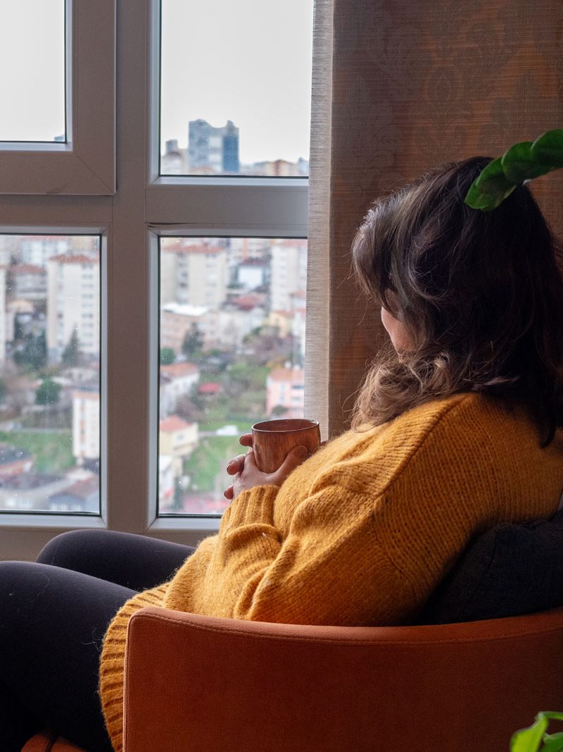 Women looking out of upper storey window onto residential area holding a cup
